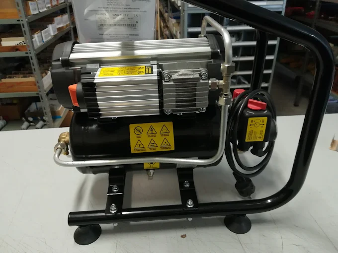 Compressore compatto con motore in alluminio alettato, serbatoio nero, telaio tubolare ed etichette gialle di sicurezza