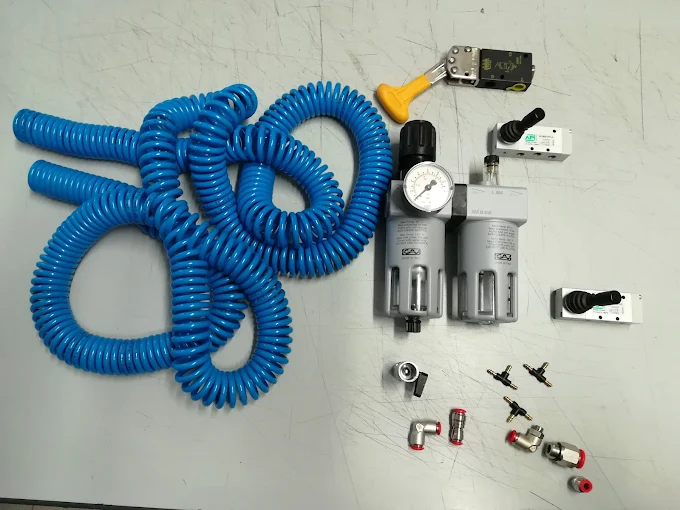 Tubi spiralati blu, gruppo filtro regolatore con manometro, valvole a leva e raccordi pneumatici su banco grigio